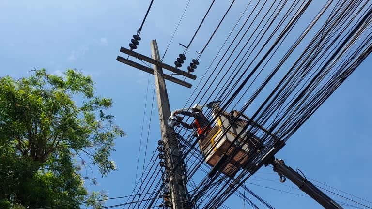 Lineman working on a utility pole, inspecting tools during routine maintenance