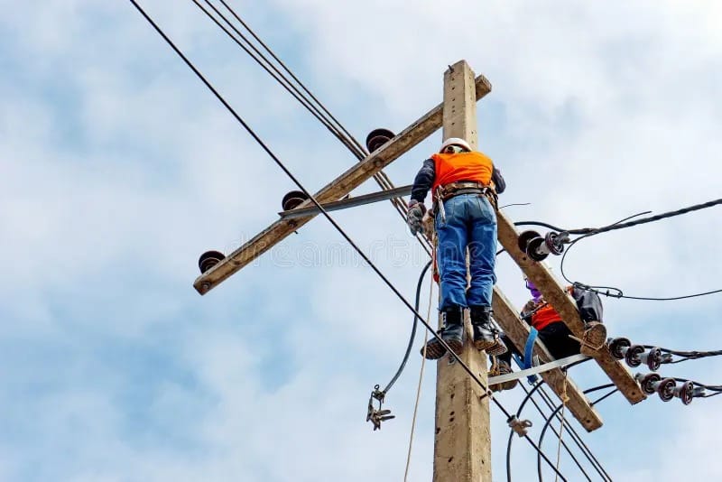 Two linemen in safety gear working together on a utility pole with climbing equipment and tools.