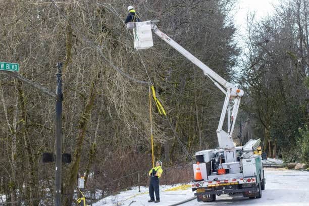 Lineman Performing Winter Line Work from Bucket Truck Utility lineman working from a bucket truck during winter conditions while ground crew supports below.