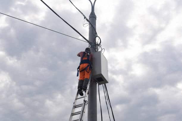 Lineman performing mid-job tool safety check while working on utility pole with climbing gear and equipment